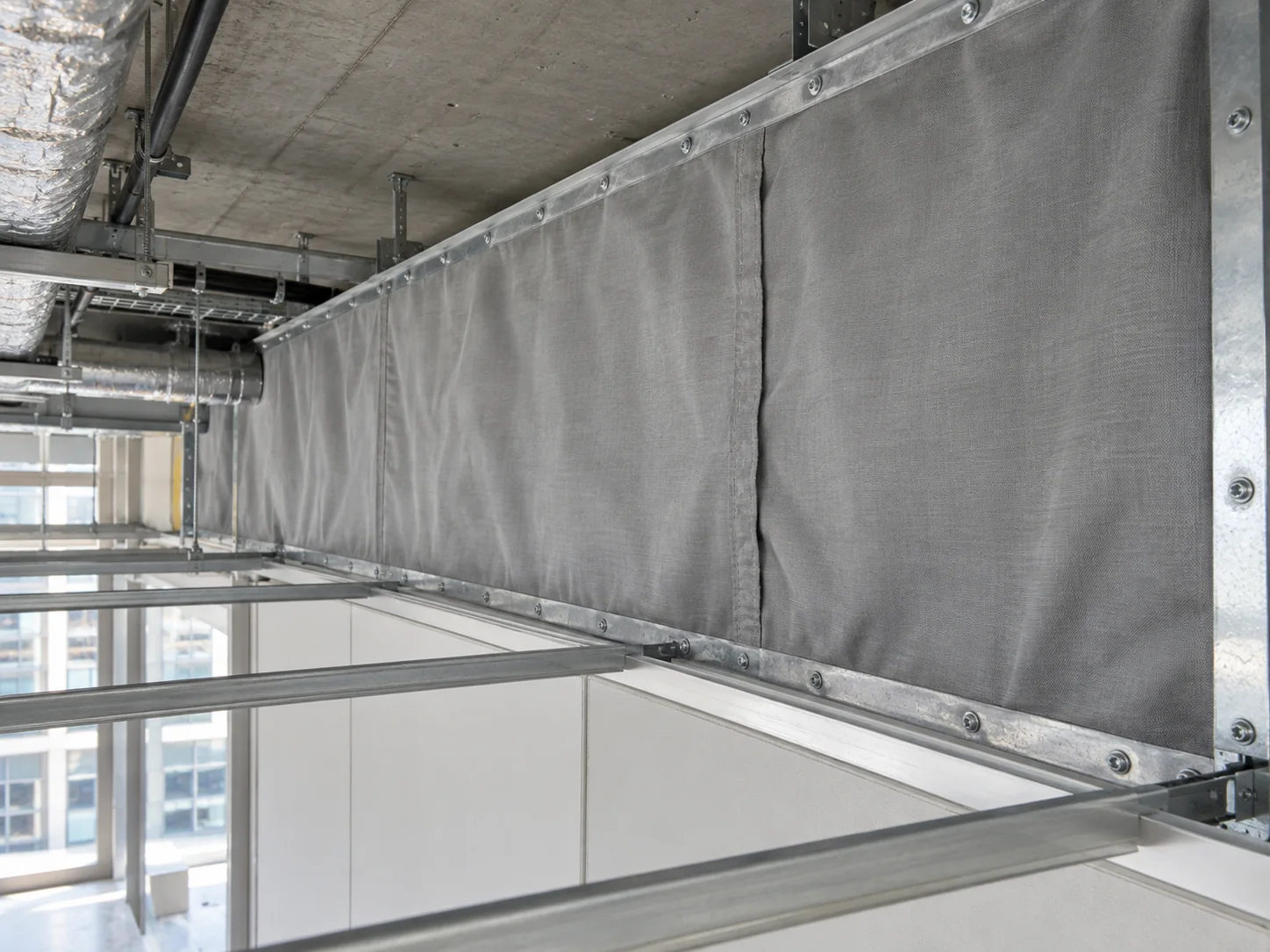 Illustrative service image: a flexible fabric fire barrier fixed to metal framing above a suspended ceiling grid.