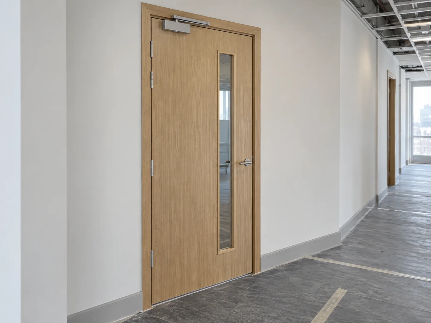 Illustrative service image: timber door with a narrow vision panel and overhead closer in an unfinished corridor.